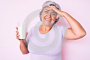 Senior hispanic woman holding glass of milk stressed and frustrated with hand on head, surprised and angry face