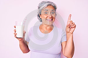 Senior hispanic woman holding glass of milk surprised with an idea or question pointing finger with happy face, number one