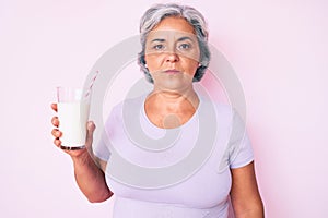 Senior hispanic woman holding glass of milk thinking attitude and sober expression looking self confident