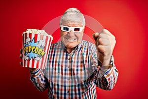 Senior hoary man watching film using 3d glasses eating popcorn over red background annoyed and frustrated shouting with anger,