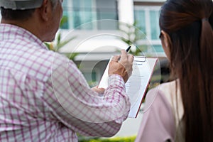 Senior home inspector explains Inspection results with homeowner, handyman holding clipboard and after checking details before