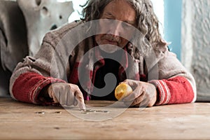 Senior homeless man eating an apple counting coins