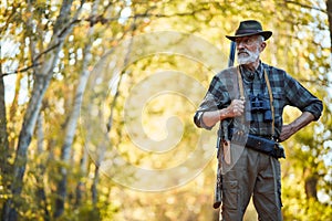 Senior hunter with shotgun in hunting clothes in autumn forest looking for trophy