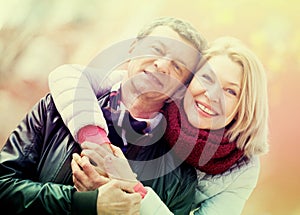 Senior husband and wife cuddling outdoors