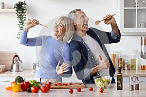 Senior husband and wife having fun while cooking, singing songs