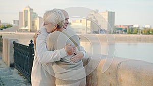 Senior husband and wife meeting at river embankment hugging talking holding hands