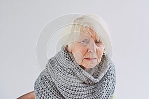 Senior ill woman in scarf freezing cold at home.