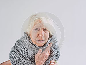 Senior ill woman in scarf freezing cold at home.