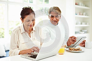 Senior Indian Couple Using Laptop And Digital Tablet At Home