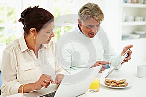 Senior Indian Couple Using Laptop And Digital Tablet At Home