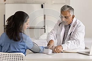 Senior Indian doctor man checking blood pressure of young woman