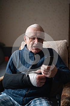 Senior with injured arm in sling browsing smartphone.