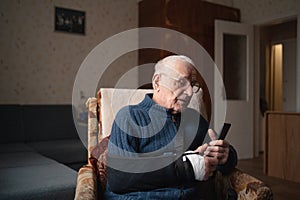 Senior with injured arm in sling browsing smartphone.