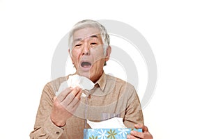 Senior Japanese man with an allergy sneezing into tissue