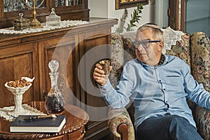 Senior Jew in armchair drinks wine in traditional home