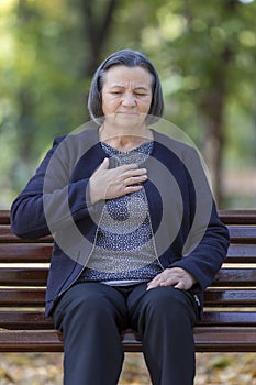 Senior lady clutching her chest in pain in park on an autumn day