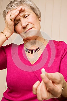 Senior lady with headache holding tablet or pill