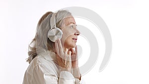 Senior lady in headphones enjoying calming music, white background, leisure concept