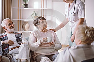 Senior lady with nurse and sitting with her elderly friends