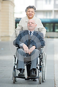 Senior lady pushing husband in wheelchair