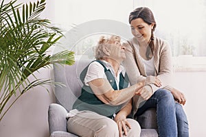 Senior lady sitting in armchair at nursing home, supporting nurse