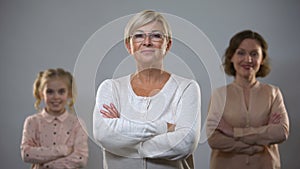 Senior lady standing with crossed arms, daughter and granddaughter on background