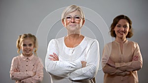 Senior lady standing with crossed arms, daughter and granddaughter on background