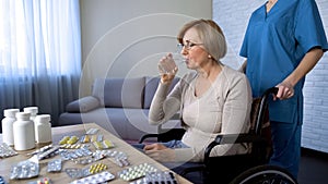 Senior lady in wheelchair at table taking medicine, treatment in nursing home