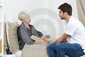 Senior lady and young male carer holding hands