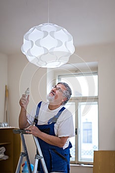 Senior landlord hanging a new light in a rental appartement