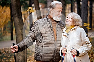 Senior lovely couple are walking together through the autumn woods, nordic walking