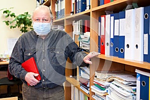 Senior male archivist holding red notebook and looking at camera, man wearing facial mask due coronavirus pandemic photo