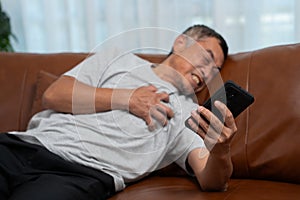 Senior male asian presses hand to his chest has a heart attack suffers from unbearable pain in the living room, lonely men try