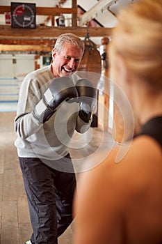 Senior Male Boxer Sparring With Younger Female Coach In Gym Using Training Gloves