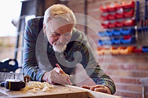 Senior Male Carpenter In Garage Workshop Measuring And Marking Piece Of Wood With Pencil