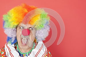 Senior male clown sticking out tongue while looking away over red background