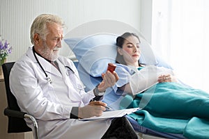 Senior male doctor checking brown medicine bottles of young patient woman in hospital bed