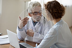 Senior male doctor consult female patient using laptop