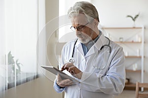 Senior male doctor using digital tablet providing online healthcare services