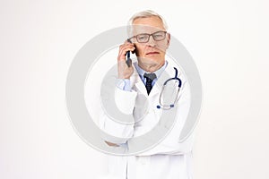 Senior male doctor using mobile phone while standing at isolated white background