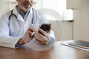 Senior male doctor using mobile phone technology apps at desk