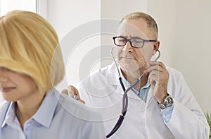 Senior male doctor using stethoscope during medical examination of woman patient