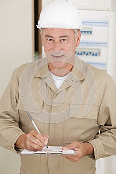 senior male electrician with clipboard by electrical fusebox