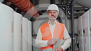 Senior male engineer in uniform standing with laptop on workshop background