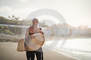 Senior male having fun surfing during sunset time - Fit retired man training with surfboard on the beach