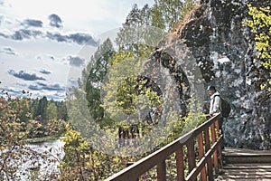 Senior male hiker admiring landscape with river on wooden hiking trail near cliff. Nature park