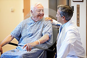 Senior Male Patient Being Pushed In Wheelchair By Doctor