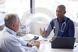 Senior Male Patient In Consultation With Doctor Sitting At Desk In Office