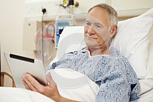 Senior Male Patient Using Digital Tablet In Hospital Bed