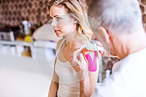 Senior male physiotherapist applying tape on a female patient. Close up.